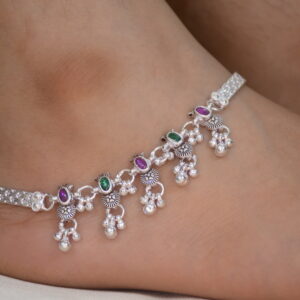 A charming silver Payal adorned with decorative purple and green stones and a ghungroo.